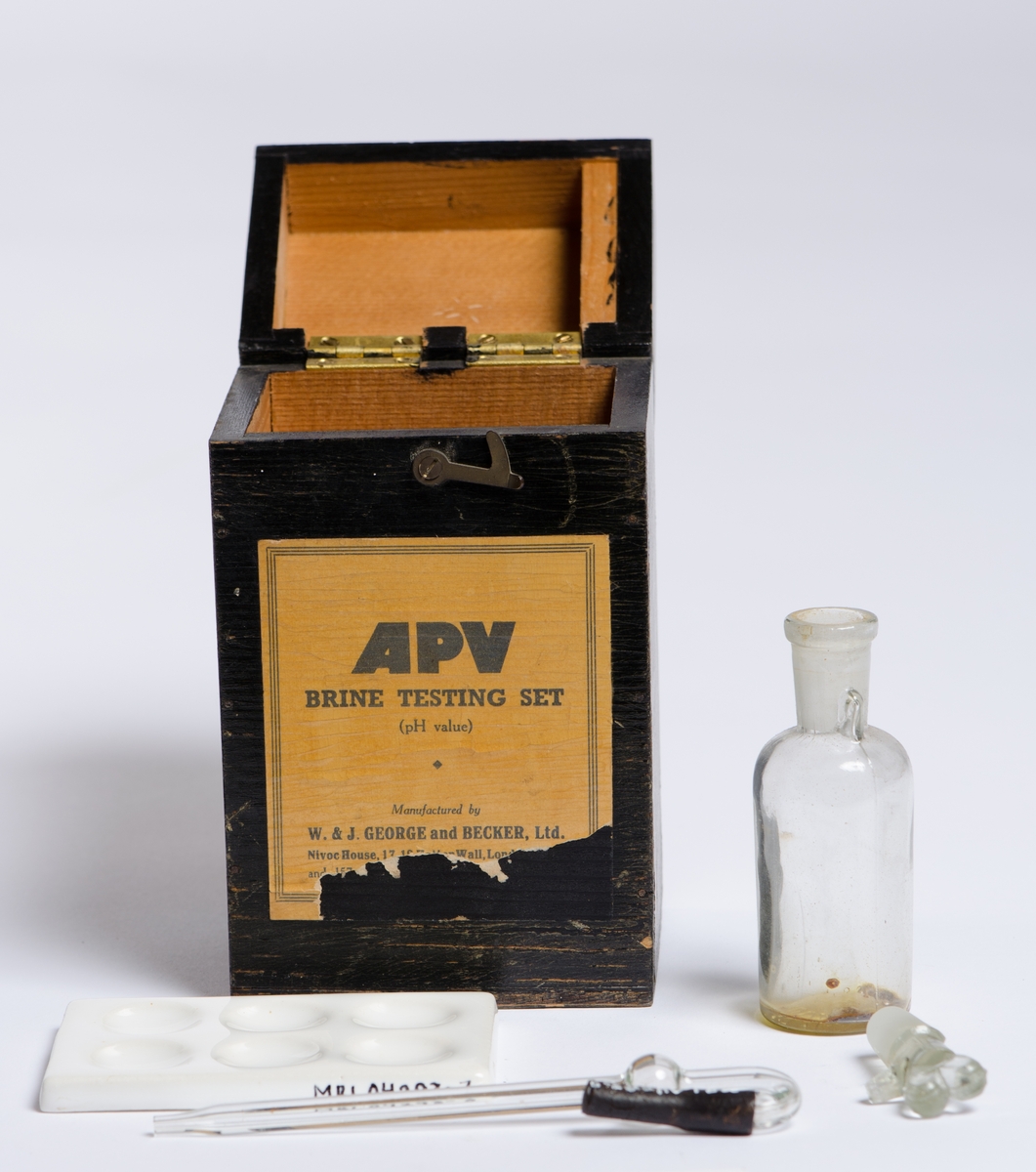 Rektangulær, sort, kube med hengslet lokk og lukkekrok. Pipette i glass med endestykke i gummi. Porselensfat med seks sirkulære fordypninger.
Kork til karaffel (selve karaffelen sitter fast i boksen) Korken er slipt i enden med gripetak formet som to ører og horisontal tapp.