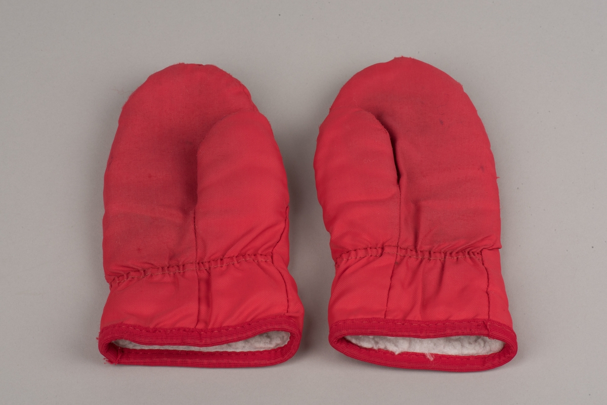 Röda tumvantar av polyester för barn av märket Helly Hansen.
Yttertyg av röd polyester och inuti ett foder av vitt fleecetyg.
På vänster vantes utsida finns Helly Hansens märke "HH" i två blåa nyanser med vit kant.
Vantarna är välanvända och jämnt slitna. De etiketter som finns inuti vantarna är blekta och svårlästa.