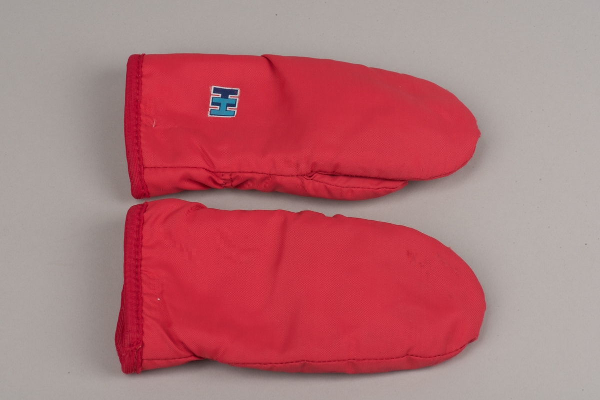 Röda tumvantar av polyester för barn av märket Helly Hansen.
Yttertyg av röd polyester och inuti ett foder av vitt fleecetyg.
På vänster vantes utsida finns Helly Hansens märke "HH" i två blåa nyanser med vit kant.
Vantarna är välanvända och jämnt slitna. De etiketter som finns inuti vantarna är blekta och svårlästa.