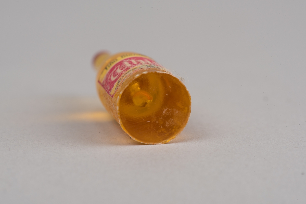 Dockskåpsinredning i form av en whiskyflaska i plast med pappersetikett.
Flaskan är gul med en röd kork. På etiketten framgår att det ska vara en whiskyflaska.