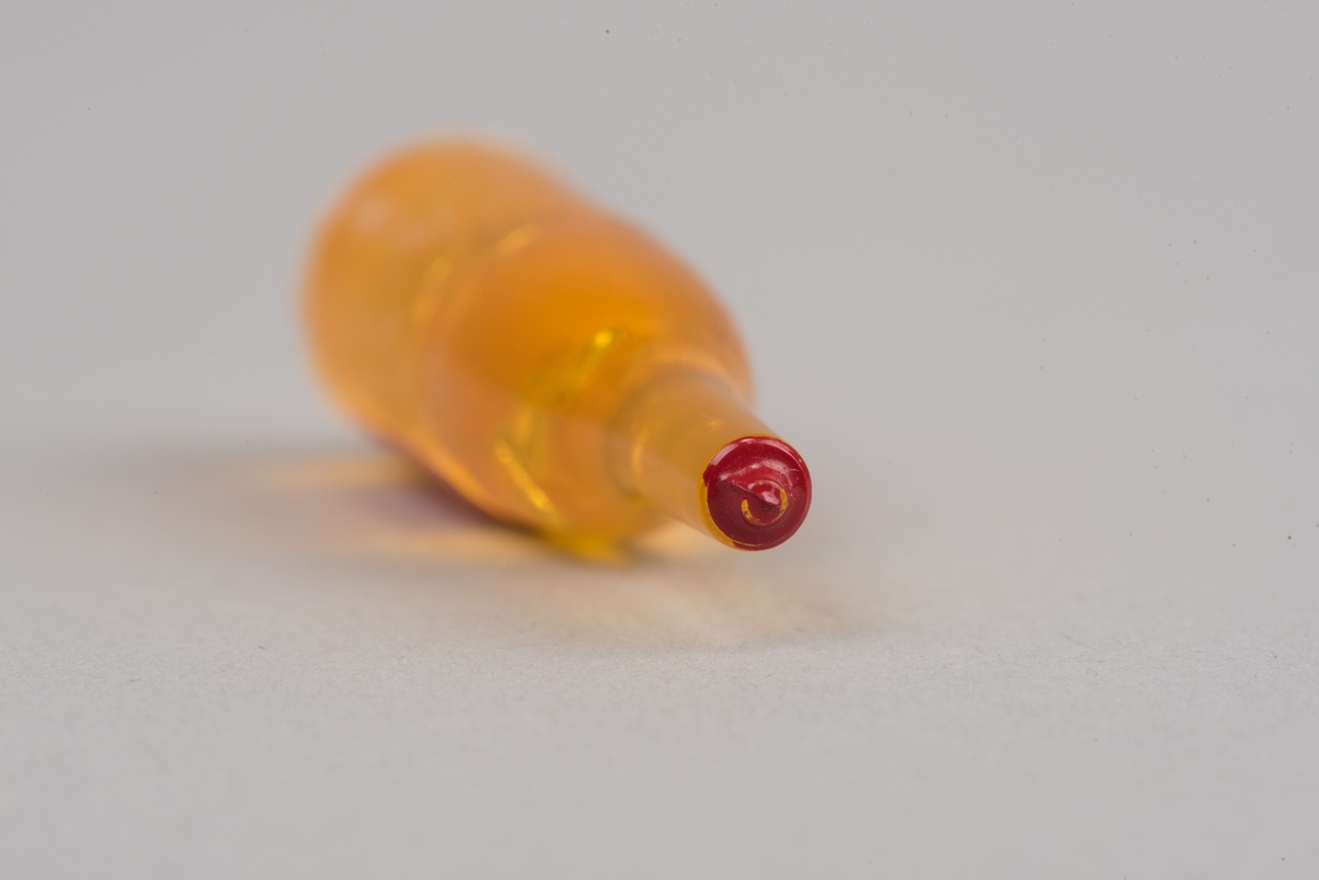 Dockskåpsinredning i form av en whiskyflaska i plast med pappersetikett.
Flaskan är gul med en röd kork. På etiketten framgår att det ska vara en whiskyflaska.