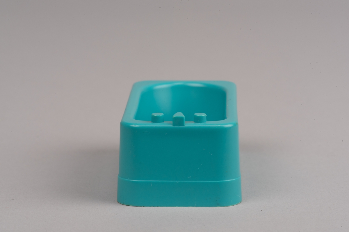 Dockskåpsmöbel i form av ett badkar tillverkat av plast.
Badkaret är rektangulärt i turkos färg. I botten finns ett avrinningshål och på den ena kortsidans övre kant sitter två kranar och en blandare, mycket förenklade i formen.