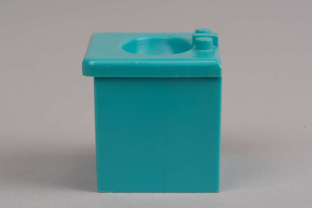 Dockskåpinredning i form av ett turkost tvättställ av plast.
Tvättstället är rektangulärt och har två dörrar på framsidan i relief. Handfatet sticker ut lite på framsidan och har en oval försänkning. Bakom denna två kranar och en blandare i förenklad form. I botten ett hål för vattenavrinning.