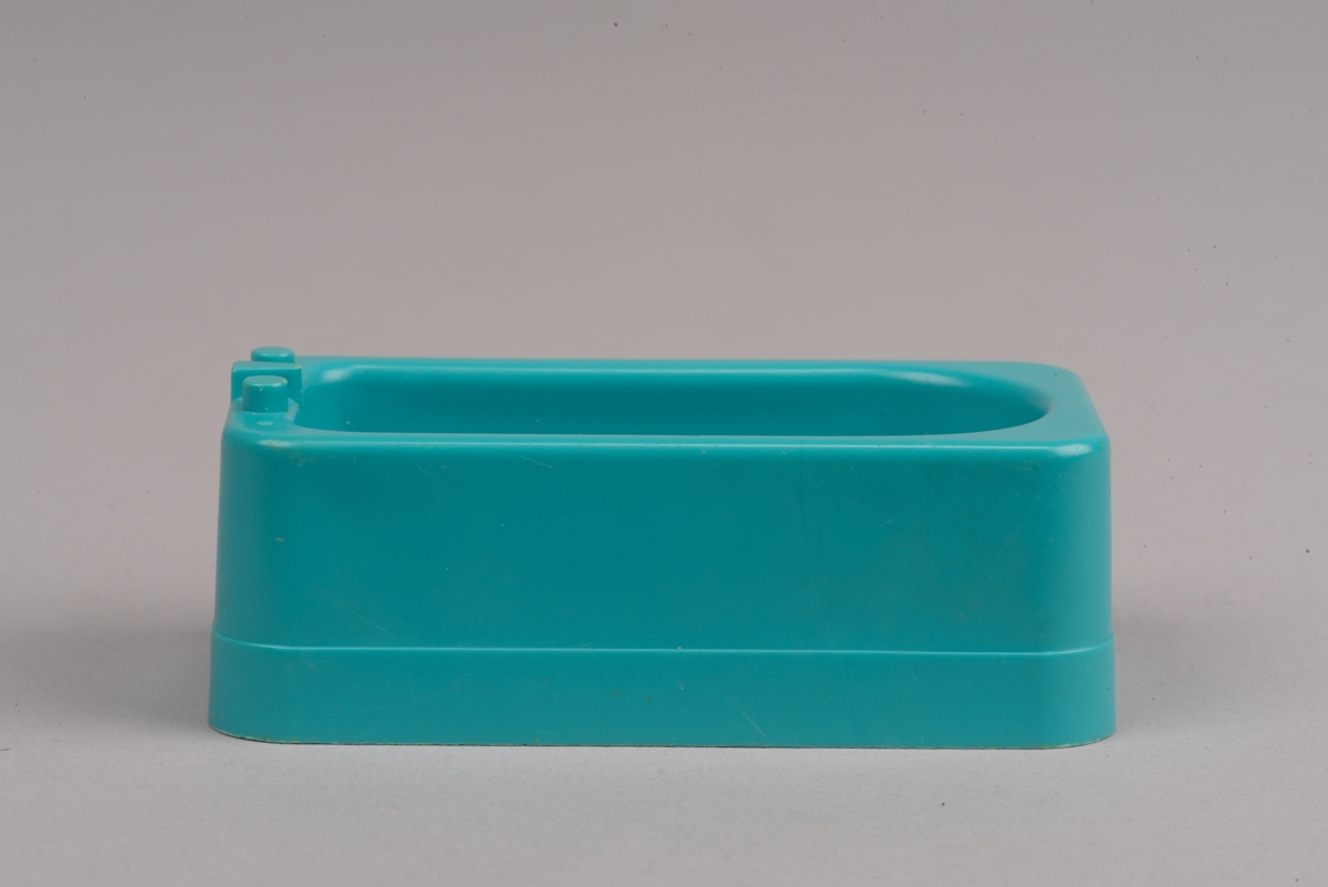 Dockskåpsmöbel i form av ett badkar tillverkat av plast.
Badkaret är rektangulärt i turkos färg. I botten finns ett avrinningshål och på den ena kortsidans övre kant sitter två kranar och en blandare, mycket förenklade i formen.