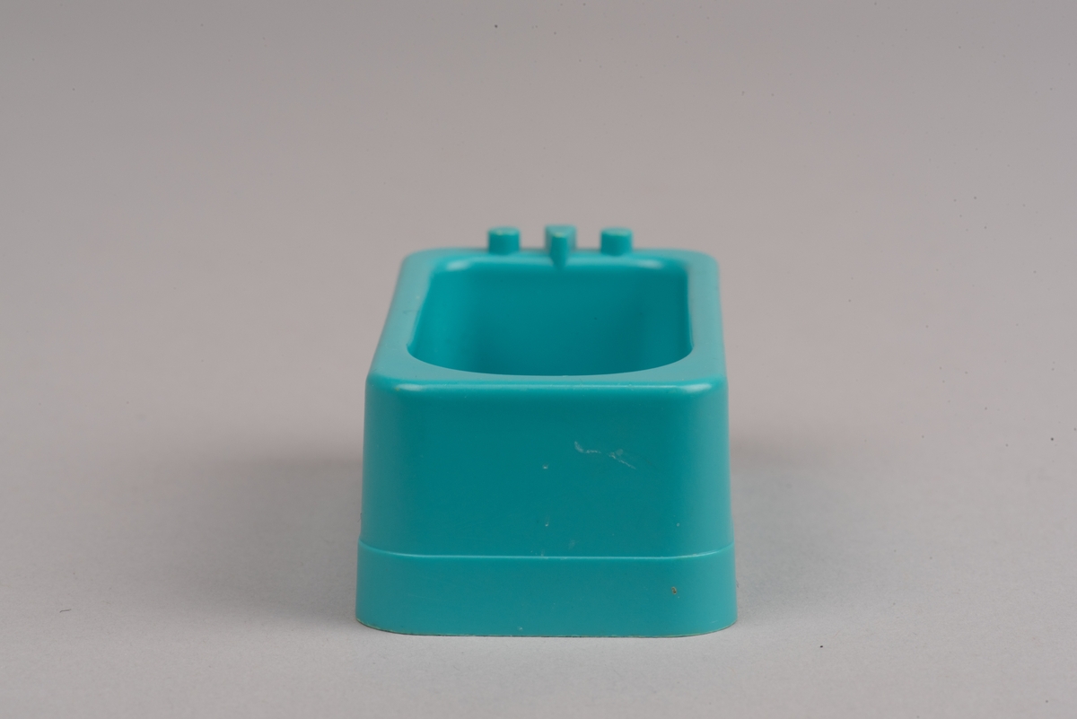 Dockskåpsmöbel i form av ett badkar tillverkat av plast.
Badkaret är rektangulärt i turkos färg. I botten finns ett avrinningshål och på den ena kortsidans övre kant sitter två kranar och en blandare, mycket förenklade i formen.