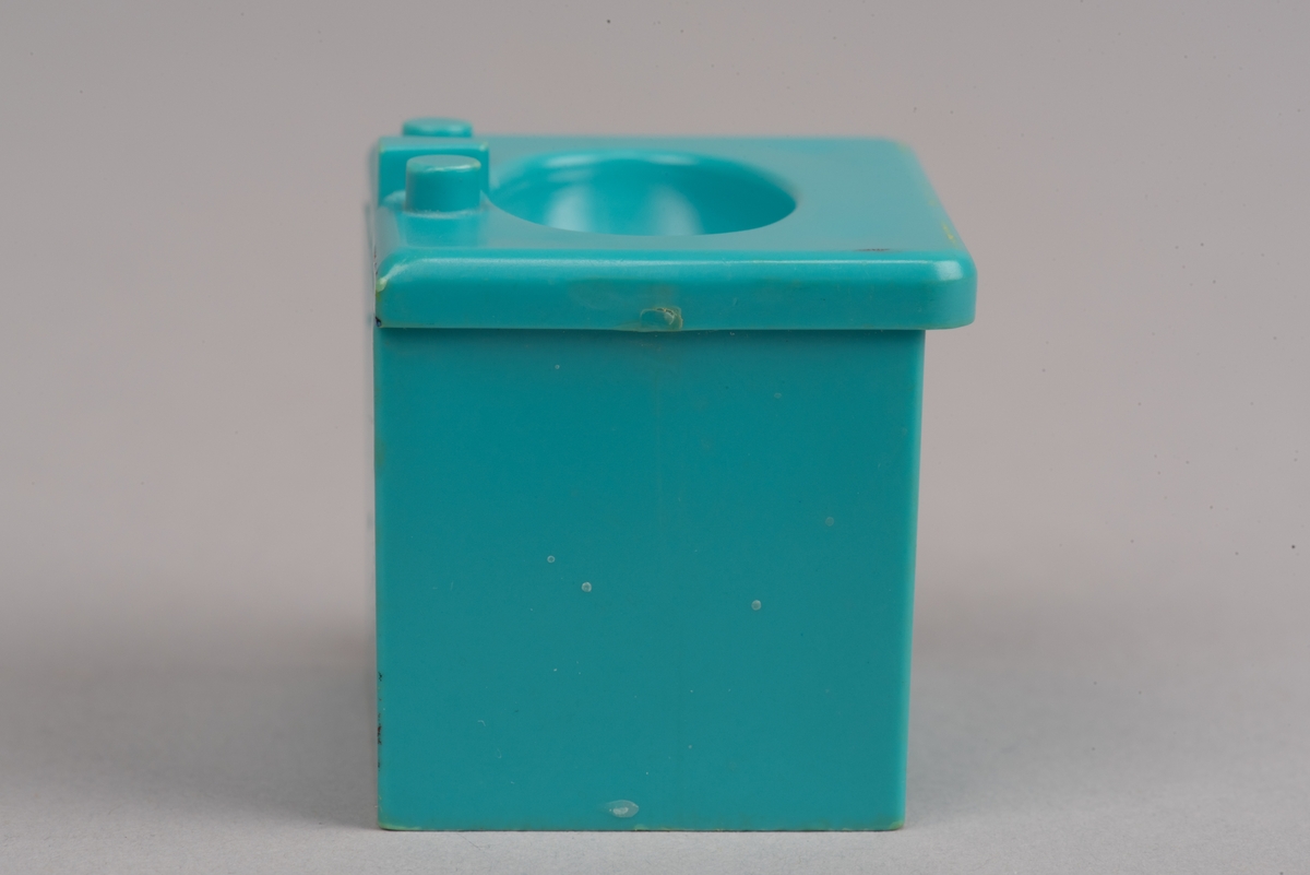 Dockskåpinredning i form av ett turkost tvättställ av plast.
Tvättstället är rektangulärt och har två dörrar på framsidan i relief. Handfatet sticker ut lite på framsidan och har en oval försänkning. Bakom denna två kranar och en blandare i förenklad form. I botten ett hål för vattenavrinning.