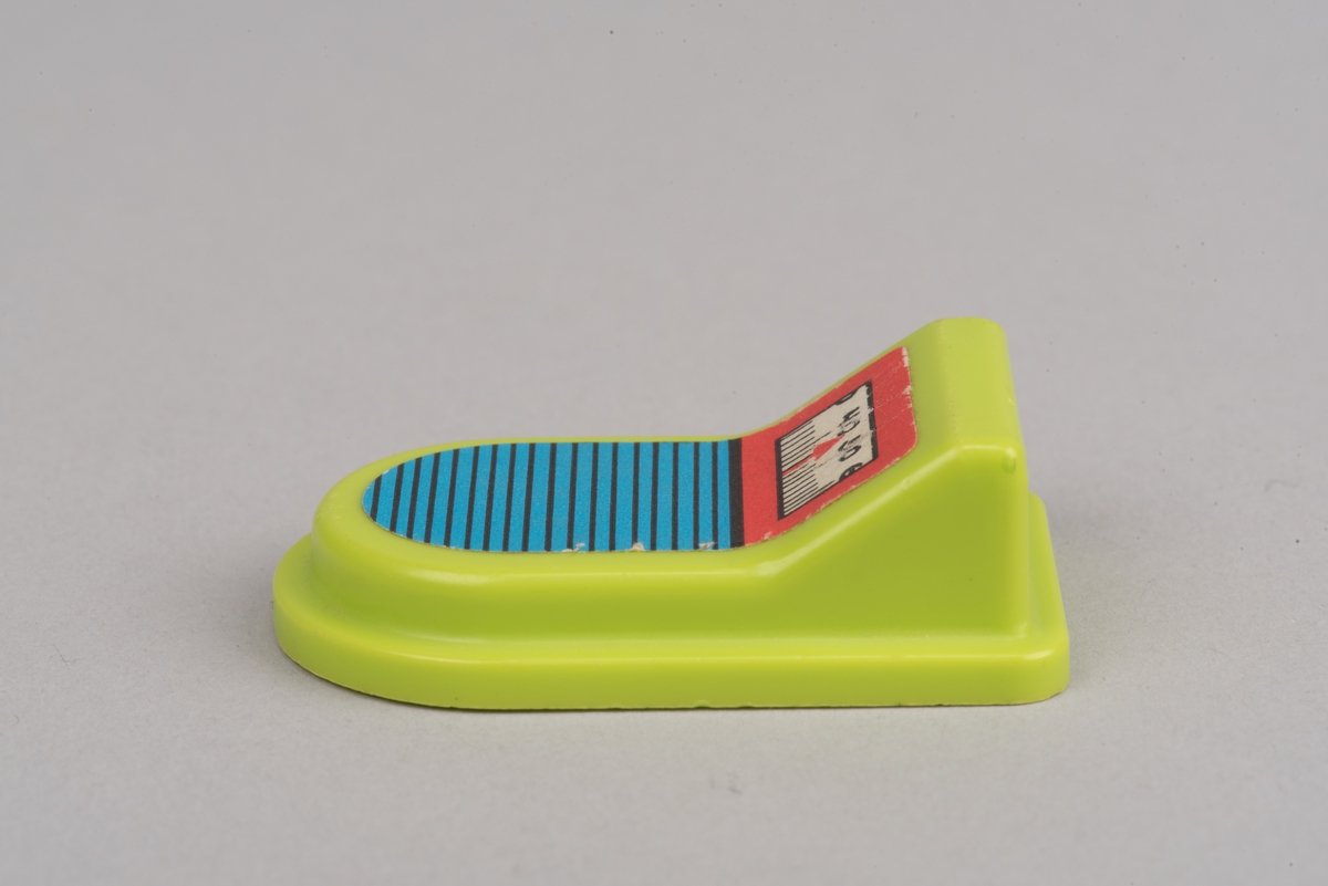 Dockskåpsinredning i form av en personvåg av gulgrön plast.
Rektangulär våg med rundad framkant och förhöjt bakstycke. På ovansidan sitter en fastlimmad etikett med en skala från 30 till 60 samt gradstreck. Själva "vågen" är blå med svarta ränder.