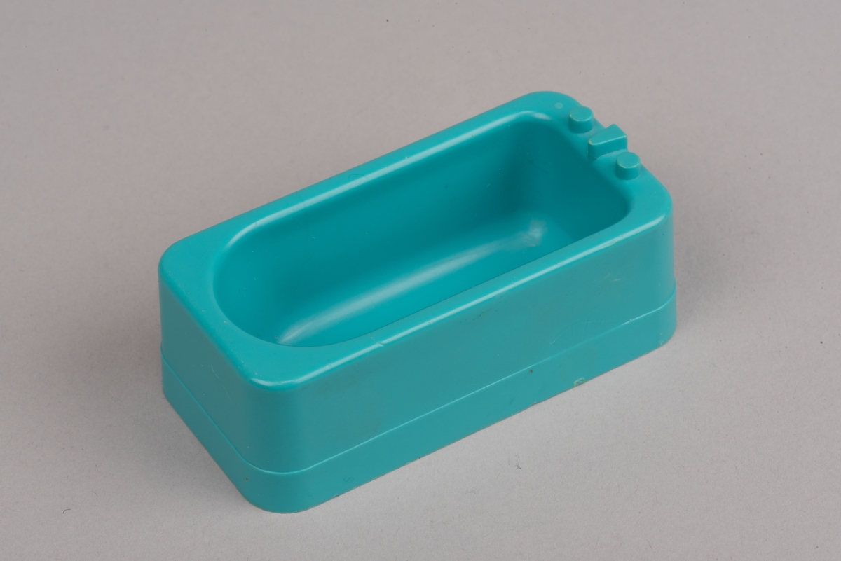 Dockskåpsmöbel i form av ett badkar tillverkat av plast.
Badkaret är rektangulärt i turkos färg. I botten finns ett avrinningshål och på den ena kortsidans övre kant sitter två kranar och en blandare, mycket förenklade i formen.