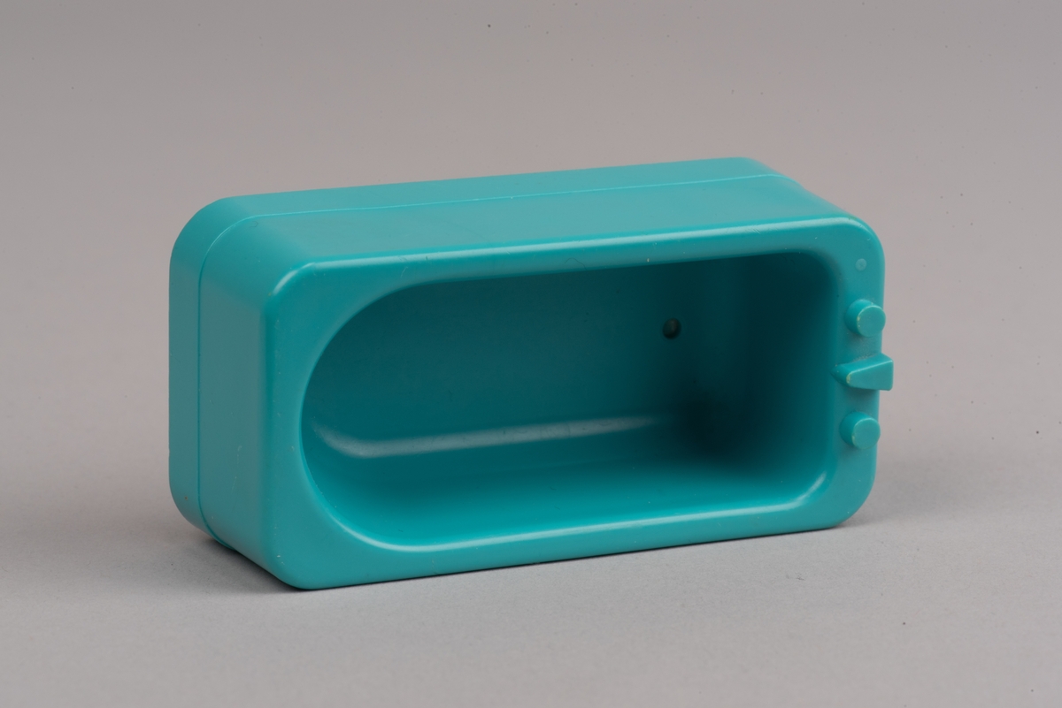 Dockskåpsmöbel i form av ett badkar tillverkat av plast.
Badkaret är rektangulärt i turkos färg. I botten finns ett avrinningshål och på den ena kortsidans övre kant sitter två kranar och en blandare, mycket förenklade i formen.