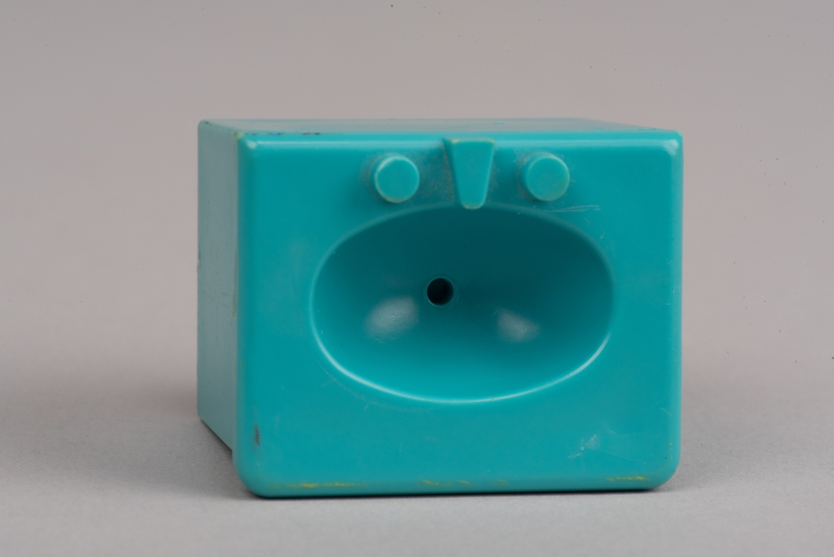 Dockskåpinredning i form av ett turkost tvättställ av plast.
Tvättstället är rektangulärt och har två dörrar på framsidan i relief. Handfatet sticker ut lite på framsidan och har en oval försänkning. Bakom denna två kranar och en blandare i förenklad form. I botten ett hål för vattenavrinning.