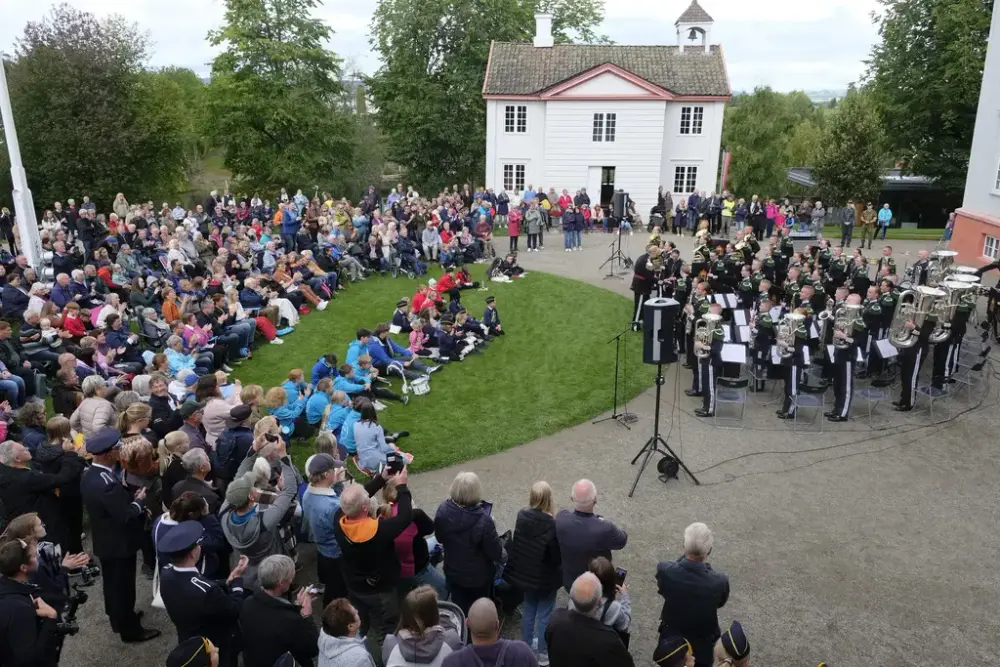 HMK Gardemusikken spiller konsert på plassen foran Eidsvollsbygnignen. Mange hundre publikummere står og sitter tett i forkant