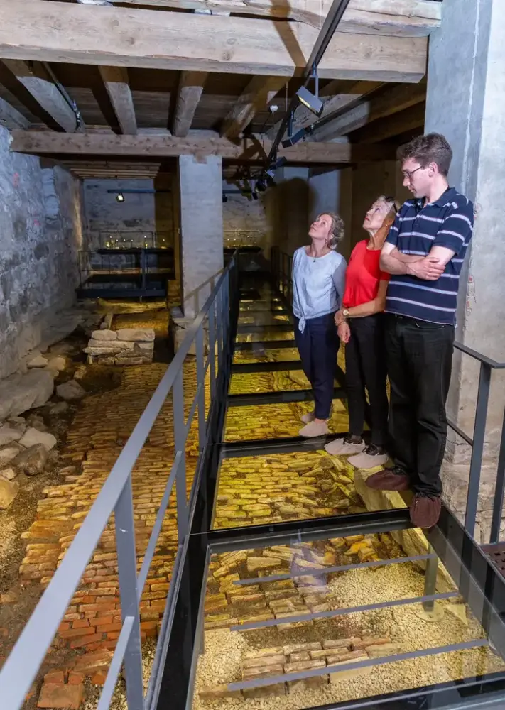 Besøkende utforsker hvelvkjelleren i Eidsvollsbygningen via en gangbro med glassgulv over historiske stein- og murstrukturer.