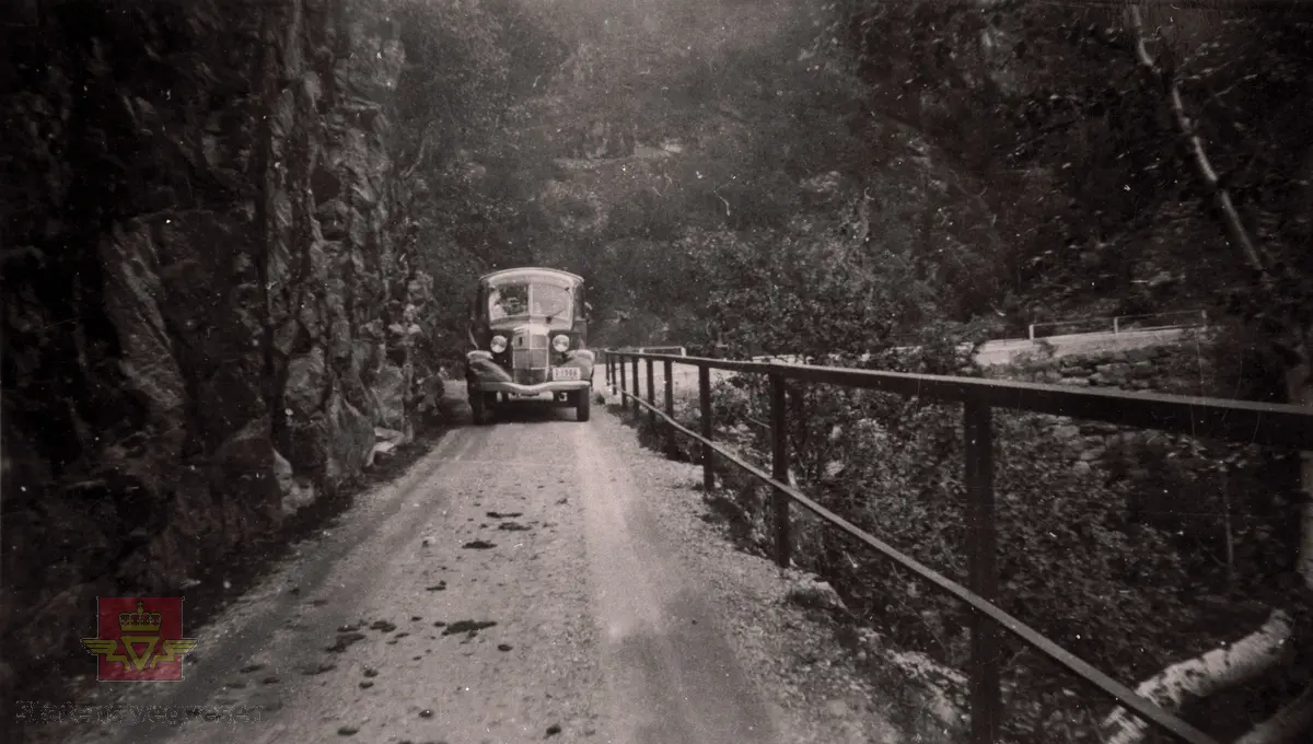 Ein rutebuss frå Firda Billag på ein smal veg med rekkverk mot gjel, ein eller annan stad i Sunnfjord i slutten av 1930-åra.

Bussen med kjenneteikn S-1566 er ein REO 1937-modell. 