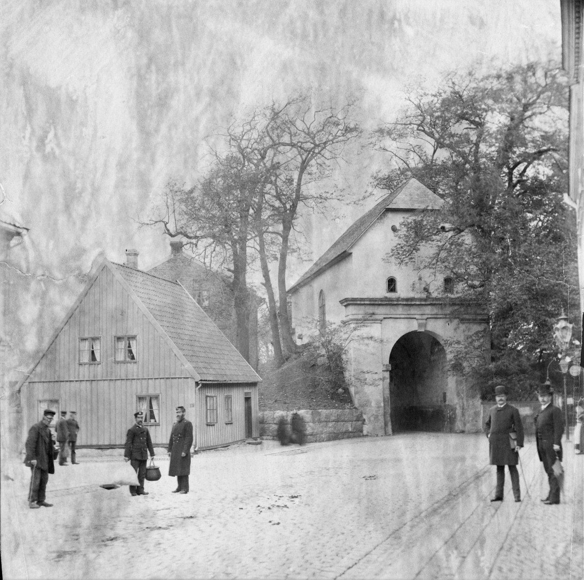 Gatubild vid Norre Port i Halmstad, sedd från Storgatan. Flera män i olika munderingar står längs vägen, vända mot fotografen. Den norra stadsporten ingick i det befästa Halmstad och stod klar 1601, alltså under danskt styre. Dess sneda vinkel gentemot Storgatan lär ha funktionen att förhindra beskjutning in mot staden. Varje natt stängdes alla stadsportarna till skydd åt invånarna. 

Stadsfullmäktige beslöt 1879 att riva portbyggnaden, men dåvarande riksantikvarien sa nej. Istället inrättade Hallands Museiförening (bildad 1886) där ett museum som öppnades 1899 och stängdes 1933. Norre Port blev byggnadsminne 2007.