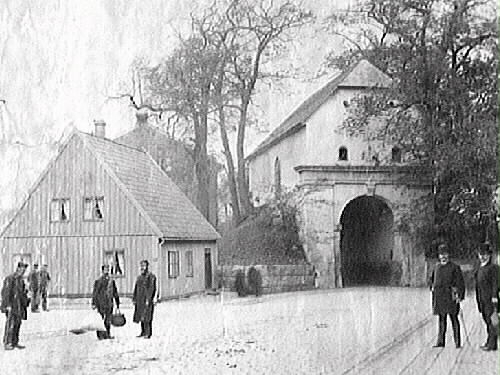 Gatubild vid Norre Port i Halmstad, sedd från Storgatan. Flera män i olika munderingar står längs vägen, vända mot fotografen. Den norra stadsporten ingick i det befästa Halmstad och stod klar 1601, alltså under danskt styre. Dess sneda vinkel gentemot Storgatan lär ha funktionen att förhindra beskjutning in mot staden. Varje natt stängdes alla stadsportarna till skydd åt invånarna. 

Stadsfullmäktige beslöt 1879 att riva portbyggnaden, men dåvarande riksantikvarien sa nej. Istället inrättade Hallands Museiförening (bildad 1886) där ett museum som öppnades 1899 och stängdes 1933. Norre Port blev byggnadsminne 2007.