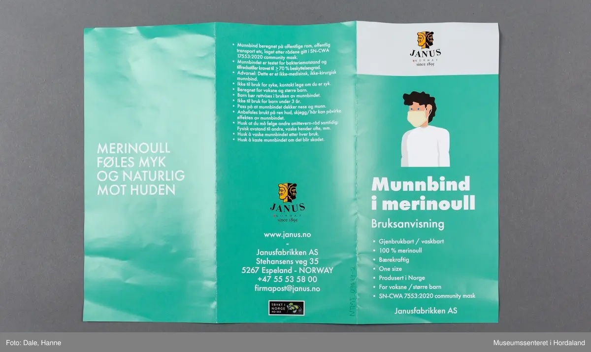 Munnbind i fleire lag strikka stoff i merinoull, med Janus- merke og elastiske stroppar til å feste det med. Munnbindet er pakka i plastemballasje med knappelukking, og det er lagt ved eit informasjonshefte om korleis ein skal bruke det.