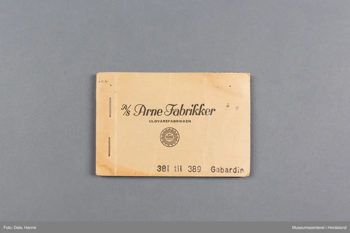 Mappe med rektangulære stoffprøver av vevd ullstoff (Gabardin) frå ullvarefabrikken ved Arne Fabrikker.