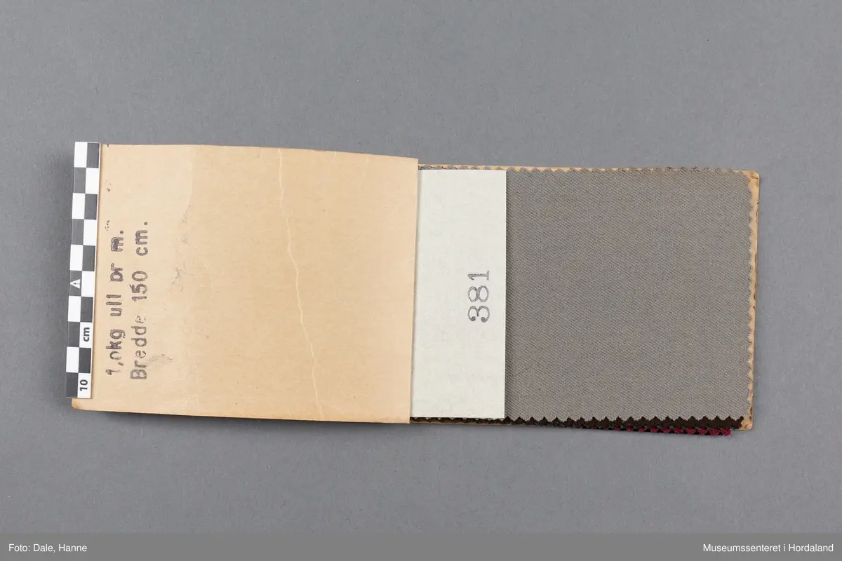 Mappe med rektangulære stoffprøver av vevd ullstoff (Gabardin) frå ullvarefabrikken ved Arne Fabrikker.