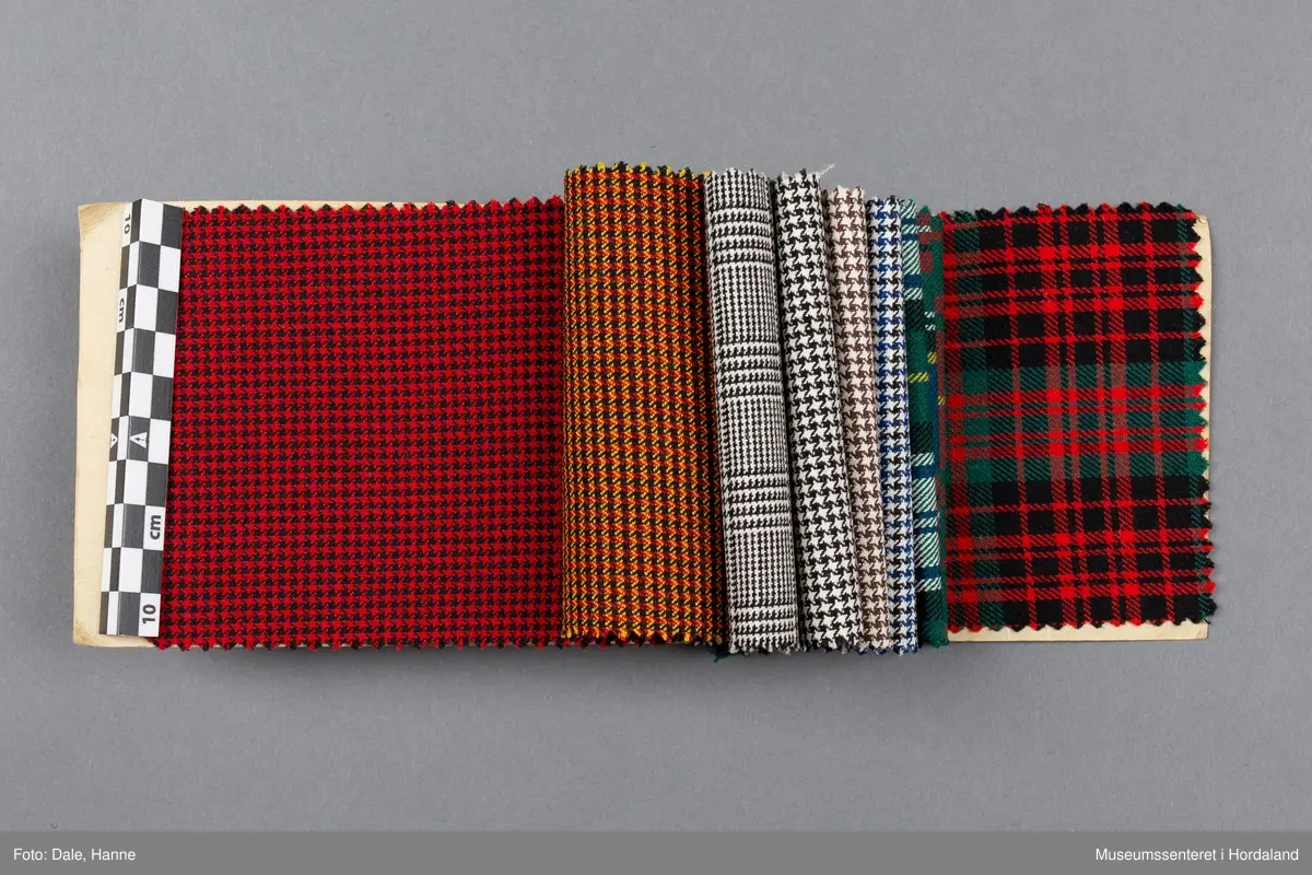 Mappe med rektangulære stoffprøver av vevd ullstoff frå ullvarefabrikken ved Arne Fabrikker. Desse er til kjoletøy i houndstooth/tartan-mønster.