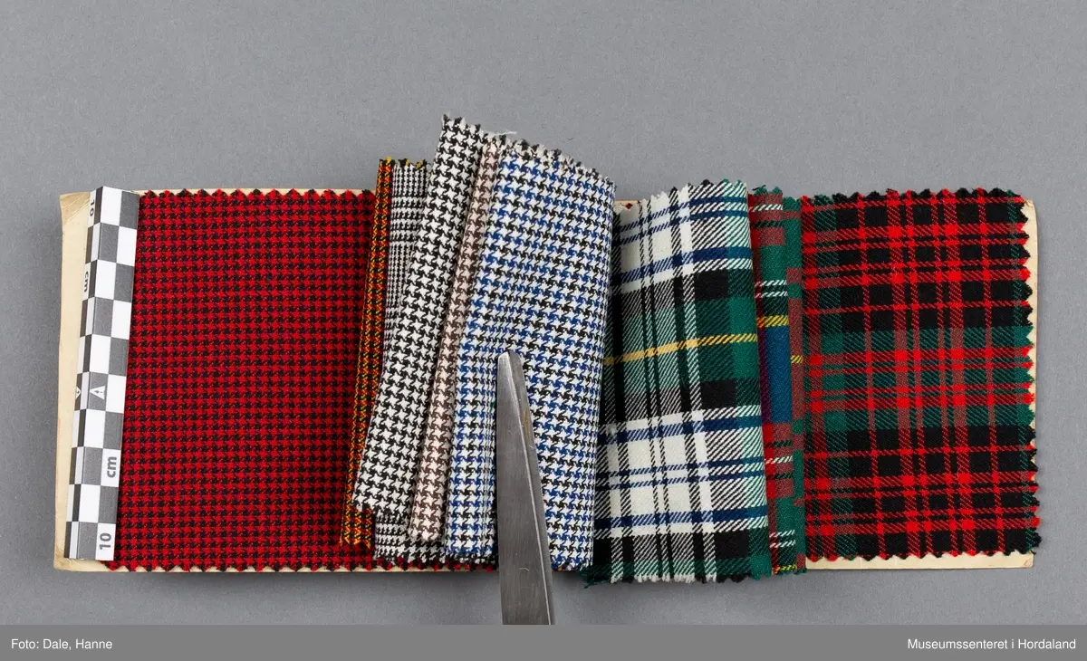 Mappe med rektangulære stoffprøver av vevd ullstoff frå ullvarefabrikken ved Arne Fabrikker. Desse er til kjoletøy i houndstooth/tartan-mønster.