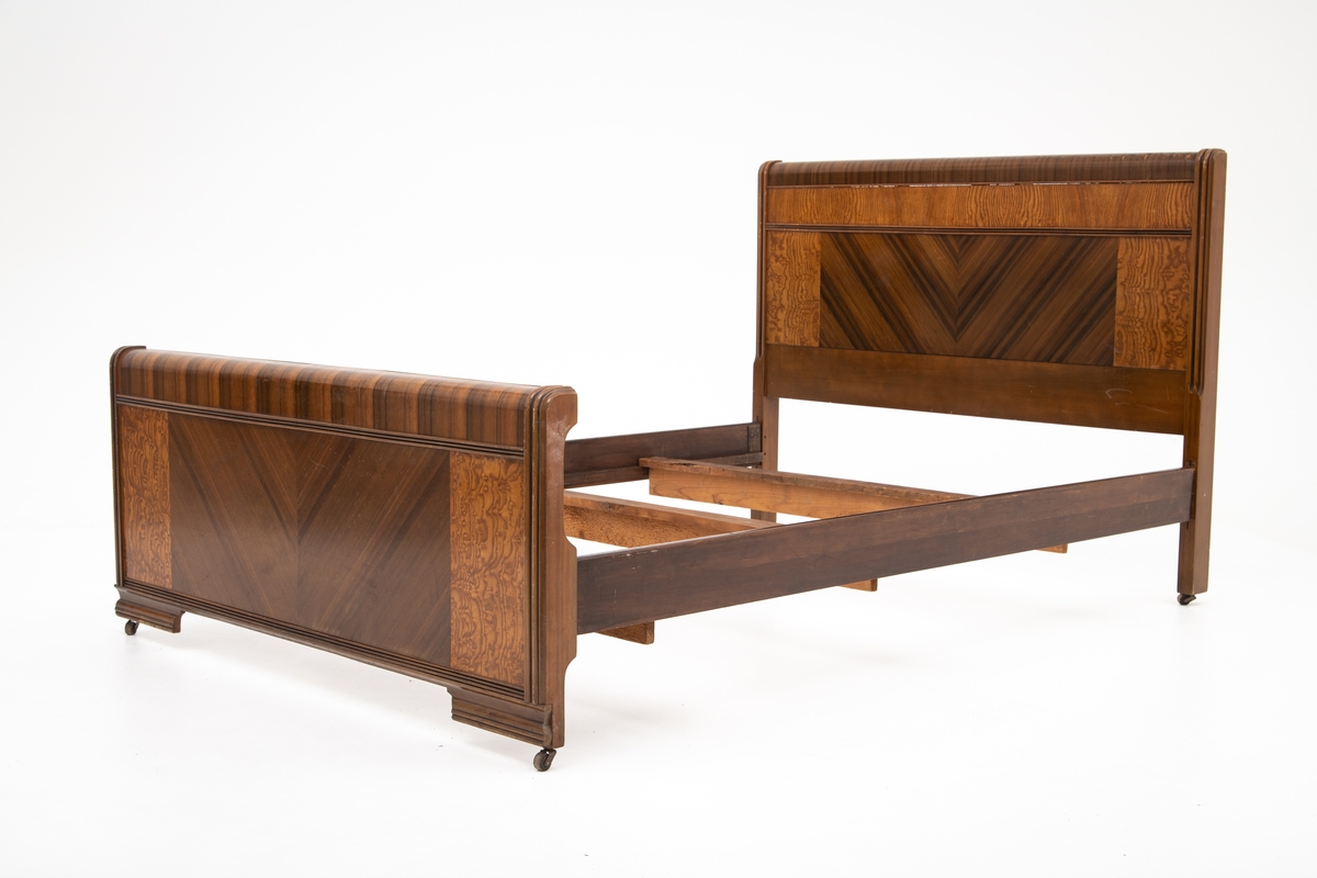 Seng i Art Deco stil. Består av hodegavl, endegavl, to sidestykker og tre tverrstykker til sengebunn. Hodegavlen er høyere enn endegavlen. Gavlstykkene er dekorert med felt i ulike typer finér, antatt bjørk og mahogni. Gavlene har avrundet kant på toppen i mørk finér, et felt med mørk finér i senter med finéren lagt i fiskebensmønster, som er rammet inn av et felt med lysere finér på hver side. Benene har påmontert små hjul. Skadet finér på hodegavl.
