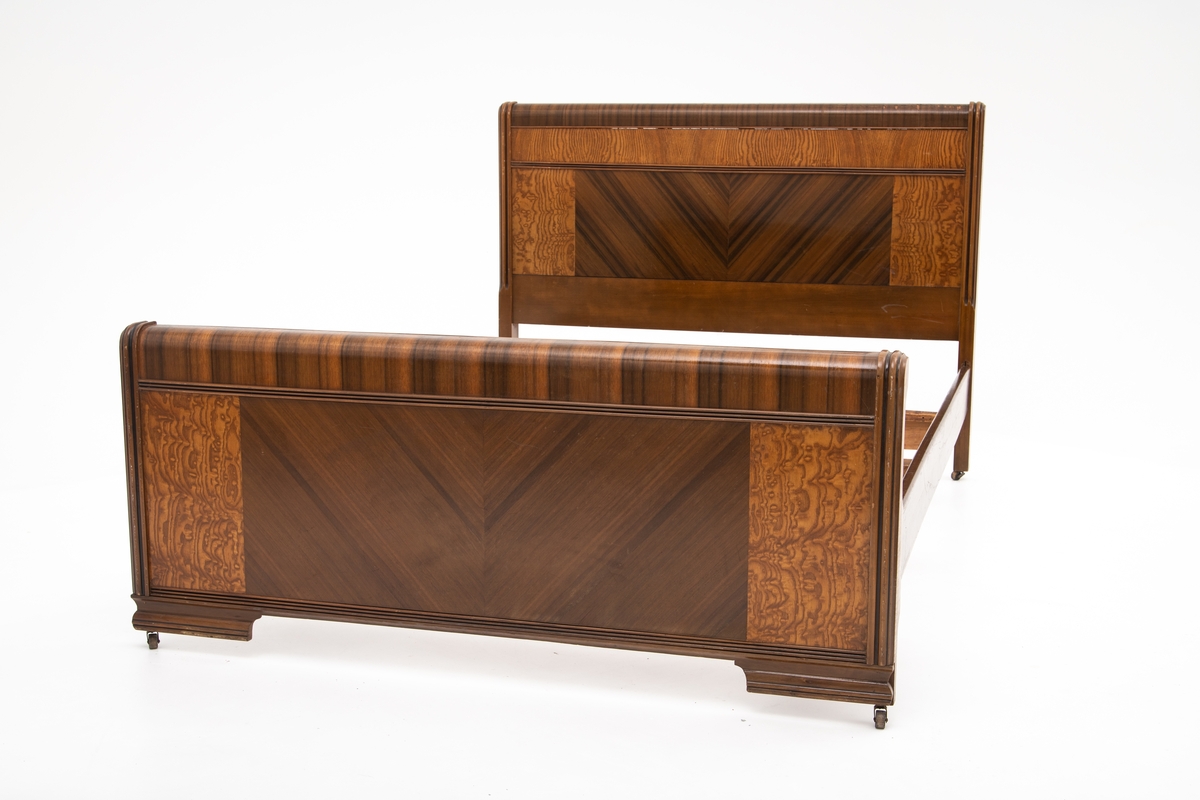 Seng i Art Deco stil. Består av hodegavl, endegavl, to sidestykker og tre tverrstykker til sengebunn. Hodegavlen er høyere enn endegavlen. Gavlstykkene er dekorert med felt i ulike typer finér, antatt bjørk og mahogni. Gavlene har avrundet kant på toppen i mørk finér, et felt med mørk finér i senter med finéren lagt i fiskebensmønster, som er rammet inn av et felt med lysere finér på hver side. Benene har påmontert små hjul. Skadet finér på hodegavl.