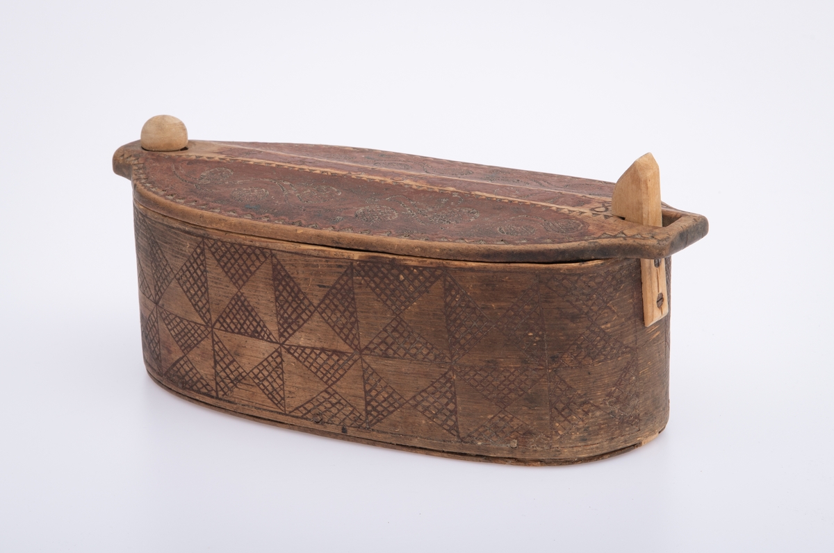 Furu, Furuspon bøyd kring oval botn og sydd manneh
med tæger. Skåret dekor, ranker og ruter. 2 jernkors mellom saumene i sida. Rep. fester for lokket. Rødmalt.