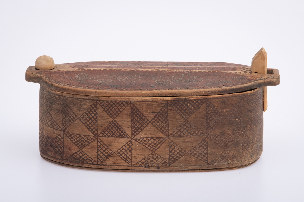 Furu, Furuspon bøyd kring oval botn og sydd manneh
med tæger. Skåret dekor, ranker og ruter. 2 jernkors mellom saumene i sida. Rep. fester for lokket. Rødmalt.