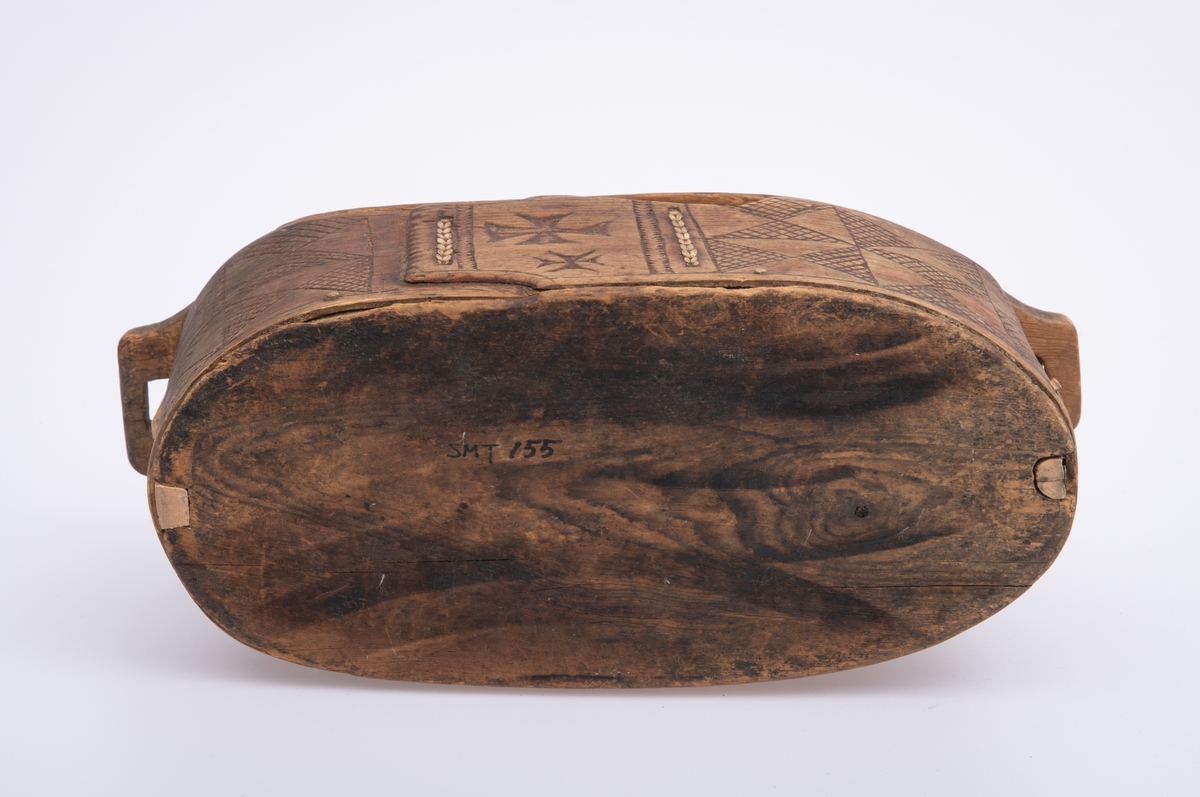 Furu, Furuspon bøyd kring oval botn og sydd manneh
med tæger. Skåret dekor, ranker og ruter. 2 jernkors mellom saumene i sida. Rep. fester for lokket. Rødmalt.