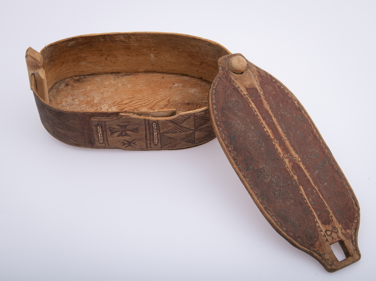 Furu, Furuspon bøyd kring oval botn og sydd manneh
med tæger. Skåret dekor, ranker og ruter. 2 jernkors mellom saumene i sida. Rep. fester for lokket. Rødmalt.