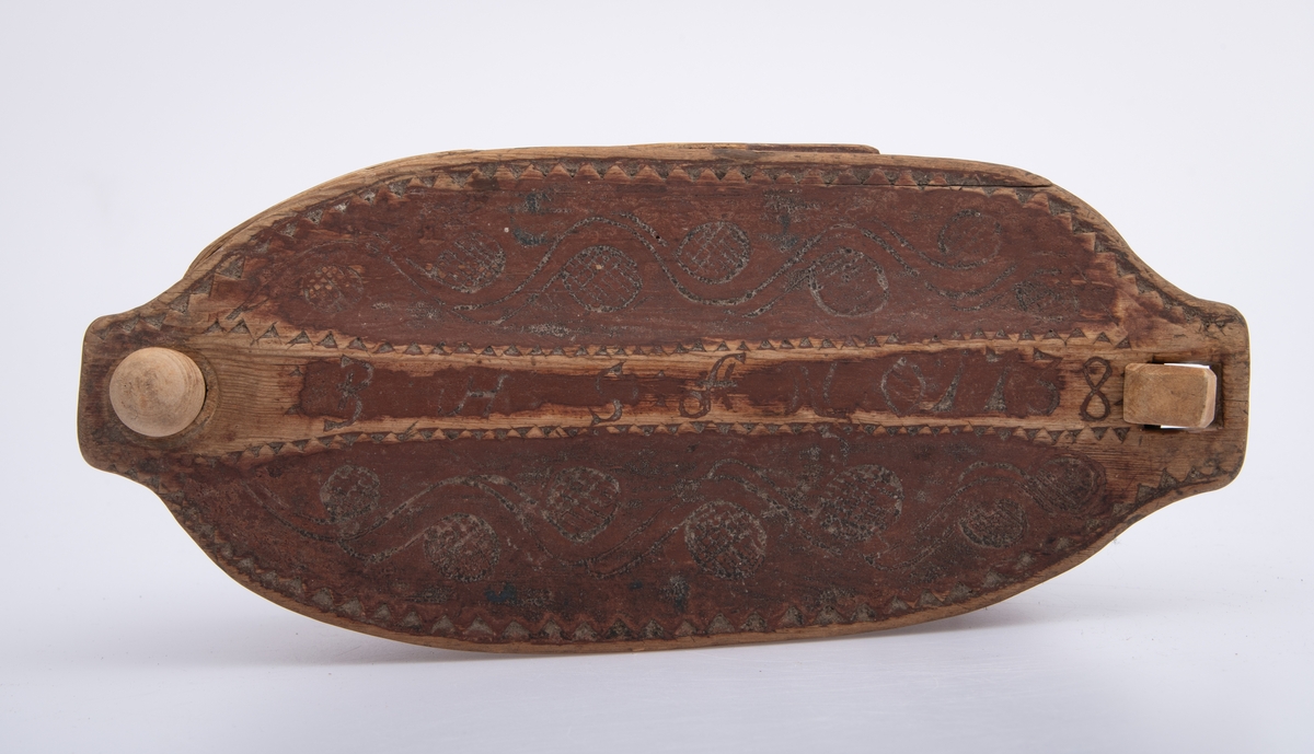 Furu, Furuspon bøyd kring oval botn og sydd manneh
med tæger. Skåret dekor, ranker og ruter. 2 jernkors mellom saumene i sida. Rep. fester for lokket. Rødmalt.