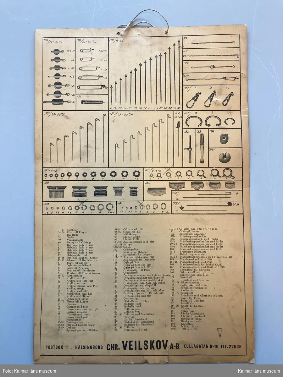 KLM 28629:558 Skylt, produktkarta. Av kartong, upptill snöre för upphängning. Karta över produkter från firman Chr. Veilskov, Helsingborg. Produkter till guldsmed såsom lås, knappar, nålar och mekanismer till olika smycken.