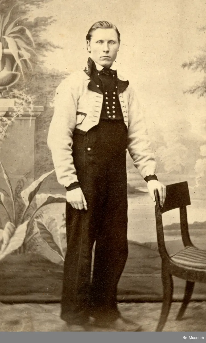 Yngre mann, fotograf Halvor H. Skogen, i gråkufte/langbukse ståande i atelier.