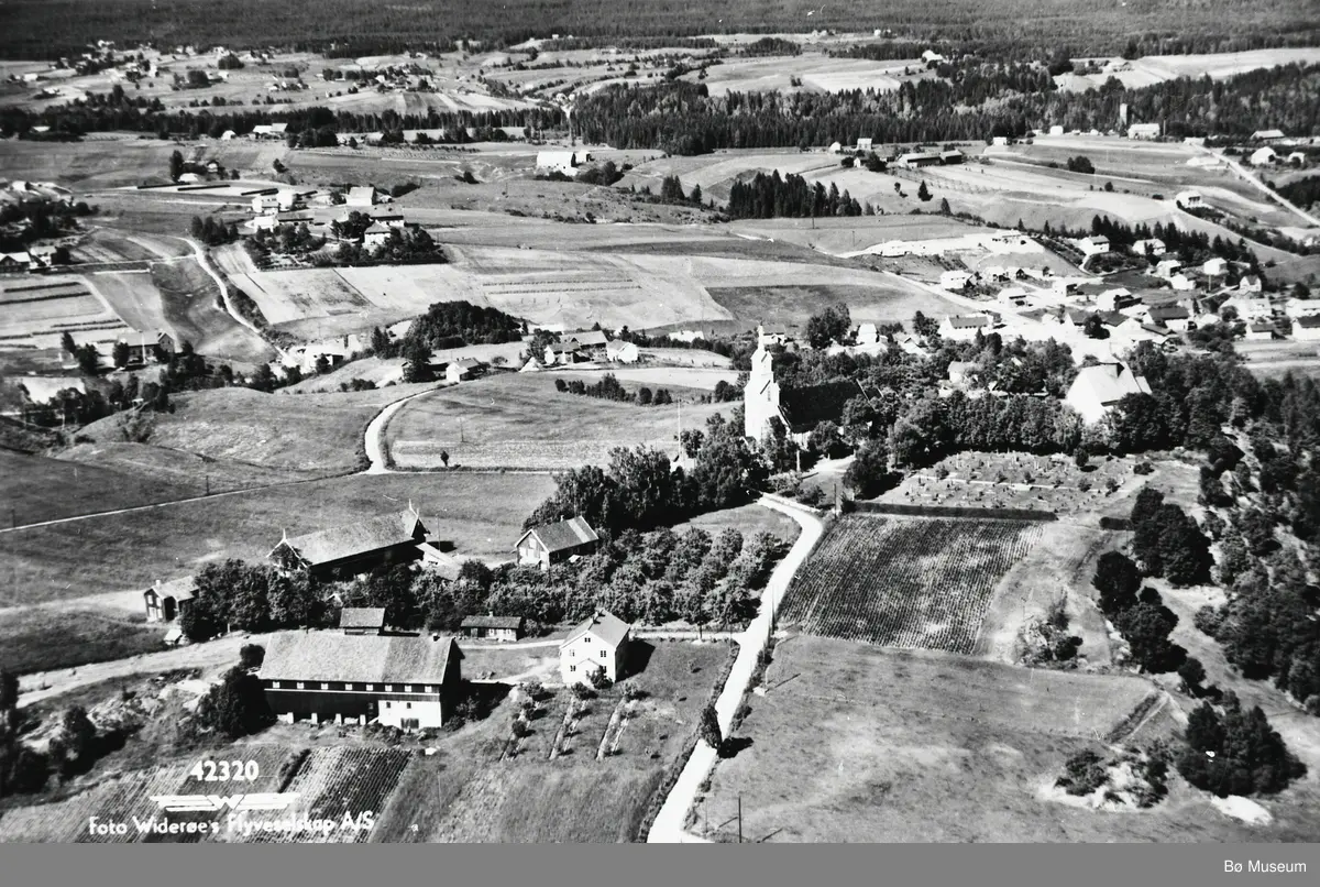 Flyfoto av Bøhaugen med kyrkjene og Midt-Bø gardane, tatt 5. juli 1952.