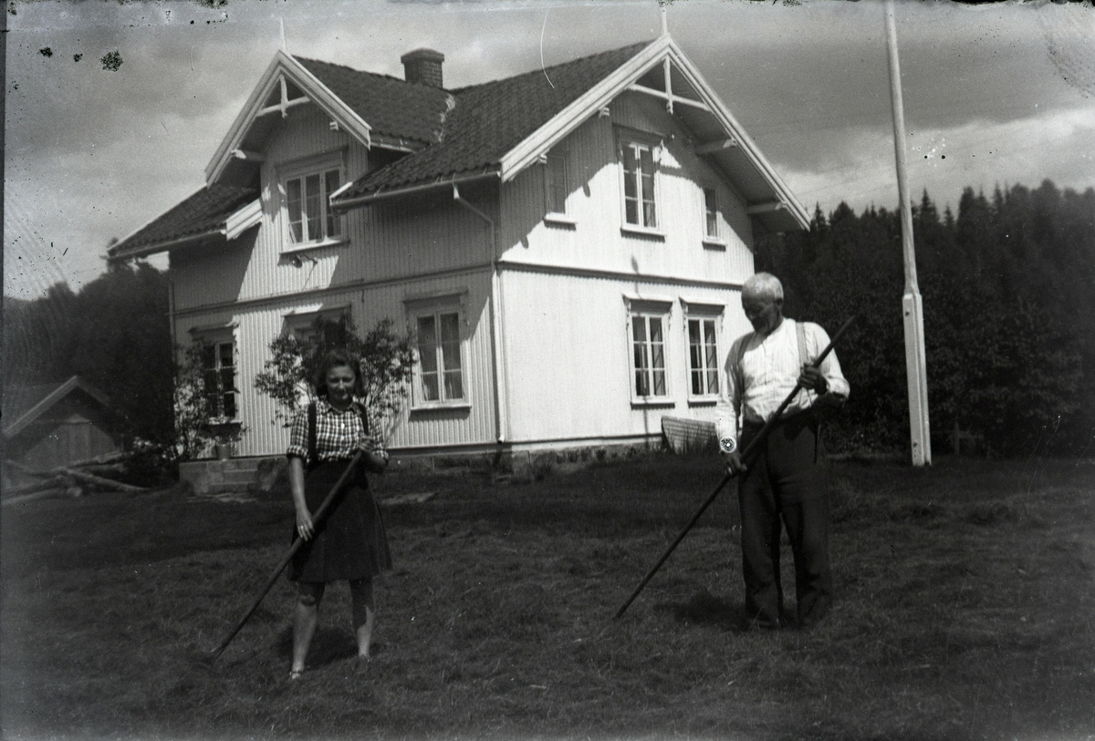 Eldre mann og yngre kvinner med ljåar utanfor eit hus.