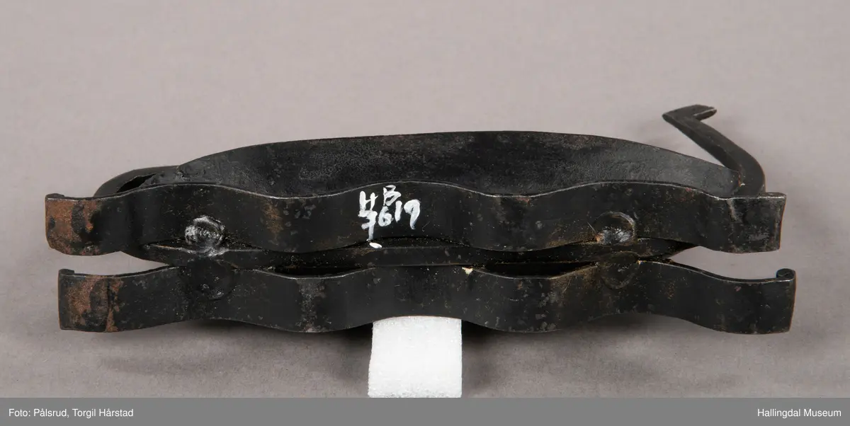 Et askebeger i form av et vikingskip plassert på to remser i jern i form av bølger. Laget av sort jern. Et enkelt utformet dragehode i baugen, i ene enden av et jernstykke som er montert på under båtformen og ender i en fremoverbøyd spiral i enden.
