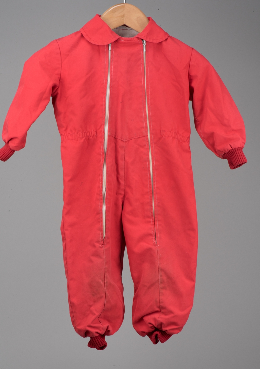 Röd bomullsoverall för barn i storlek 91.
Overallen har dubbla dragkedjor på framsidan, ärm- och benmuddar samt en rundad krage. I midjan finns ett insytt resårband.

På en etikett inuti overallen finns skötselråd men också Kooperativa förbundets symbol, oändlighetssymbolen en liggande åtta, samt "Babynett".

Overallen är välanvänd med slitna knän. De små cirkelformade märkena på overallen kommer från maskrosstjälkar. I grenen är overallen lagad, med handsydda stygn. Resåren i midjan har tappat sin spänst.