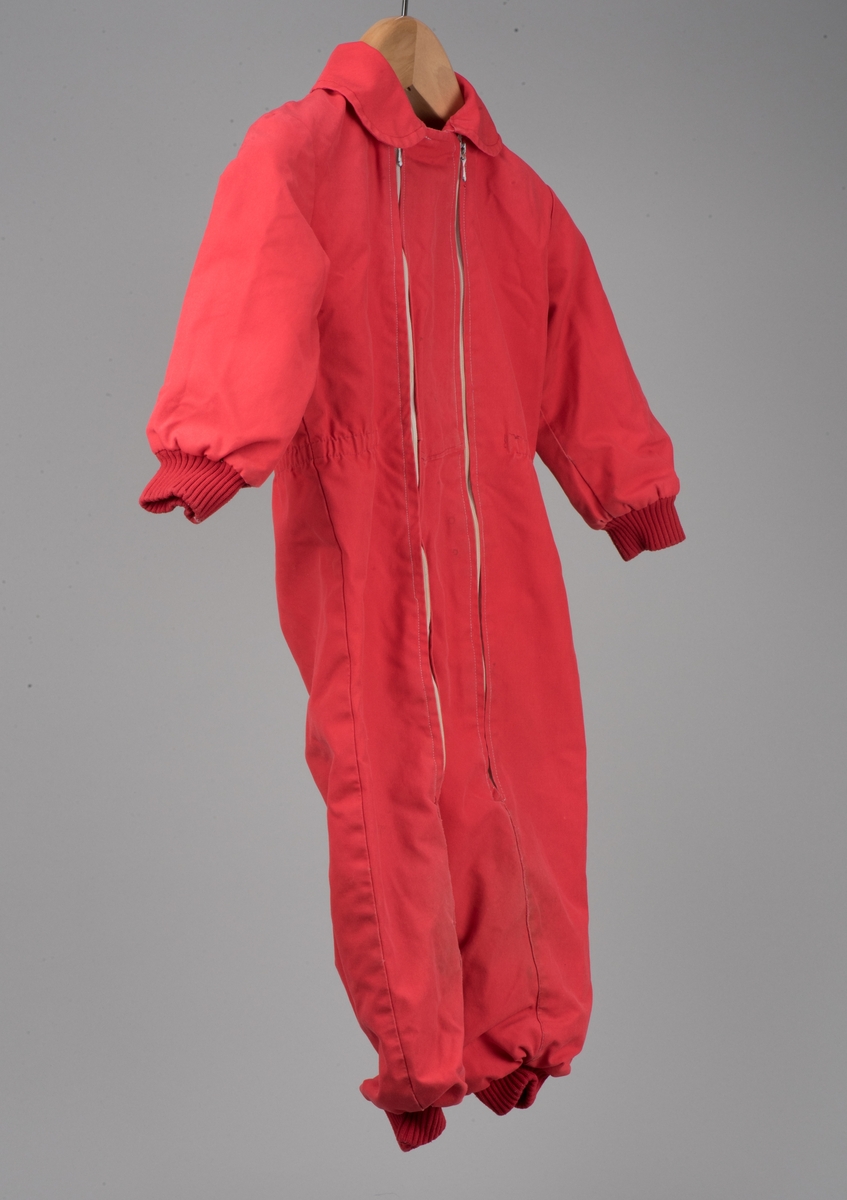 Röd bomullsoverall för barn i storlek 91.
Overallen har dubbla dragkedjor på framsidan, ärm- och benmuddar samt en rundad krage. I midjan finns ett insytt resårband.

På en etikett inuti overallen finns skötselråd men också Kooperativa förbundets symbol, oändlighetssymbolen en liggande åtta, samt "Babynett".

Overallen är välanvänd med slitna knän. De små cirkelformade märkena på overallen kommer från maskrosstjälkar. I grenen är overallen lagad, med handsydda stygn. Resåren i midjan har tappat sin spänst.