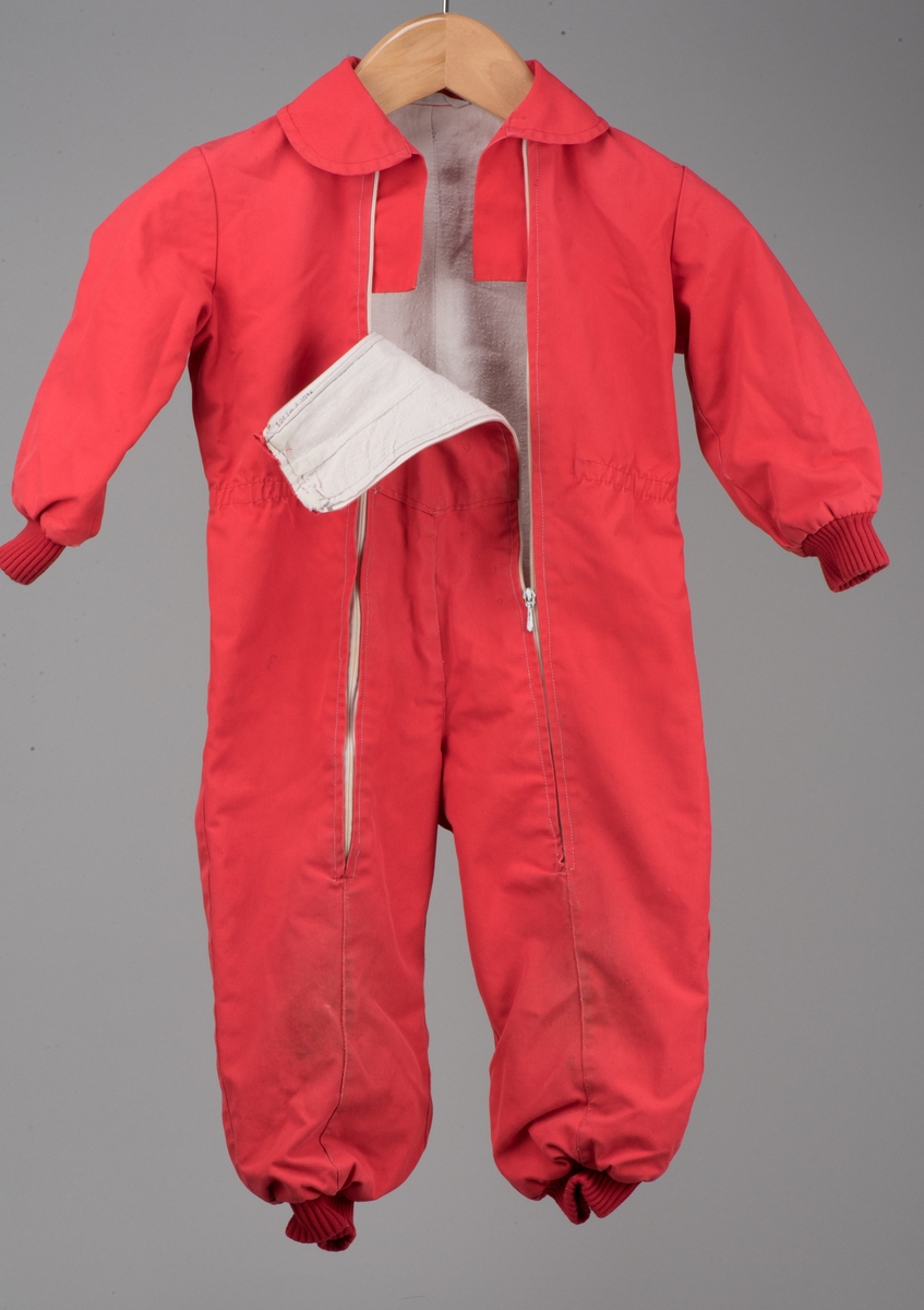 Röd bomullsoverall för barn i storlek 91.
Overallen har dubbla dragkedjor på framsidan, ärm- och benmuddar samt en rundad krage. I midjan finns ett insytt resårband.

På en etikett inuti overallen finns skötselråd men också Kooperativa förbundets symbol, oändlighetssymbolen en liggande åtta, samt "Babynett".

Overallen är välanvänd med slitna knän. De små cirkelformade märkena på overallen kommer från maskrosstjälkar. I grenen är overallen lagad, med handsydda stygn. Resåren i midjan har tappat sin spänst.
