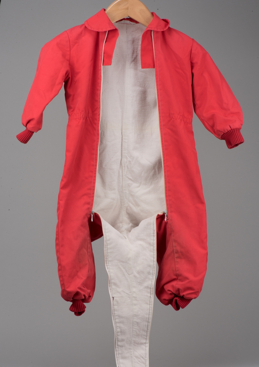 Röd bomullsoverall för barn i storlek 91.
Overallen har dubbla dragkedjor på framsidan, ärm- och benmuddar samt en rundad krage. I midjan finns ett insytt resårband.

På en etikett inuti overallen finns skötselråd men också Kooperativa förbundets symbol, oändlighetssymbolen en liggande åtta, samt "Babynett".

Overallen är välanvänd med slitna knän. De små cirkelformade märkena på overallen kommer från maskrosstjälkar. I grenen är overallen lagad, med handsydda stygn. Resåren i midjan har tappat sin spänst.