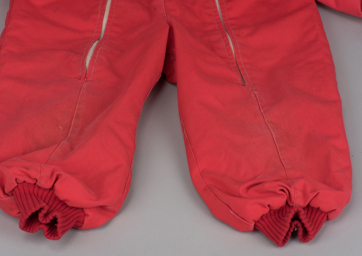 Röd bomullsoverall för barn i storlek 91.
Overallen har dubbla dragkedjor på framsidan, ärm- och benmuddar samt en rundad krage. I midjan finns ett insytt resårband.

På en etikett inuti overallen finns skötselråd men också Kooperativa förbundets symbol, oändlighetssymbolen en liggande åtta, samt "Babynett".

Overallen är välanvänd med slitna knän. De små cirkelformade märkena på overallen kommer från maskrosstjälkar. I grenen är overallen lagad, med handsydda stygn. Resåren i midjan har tappat sin spänst.