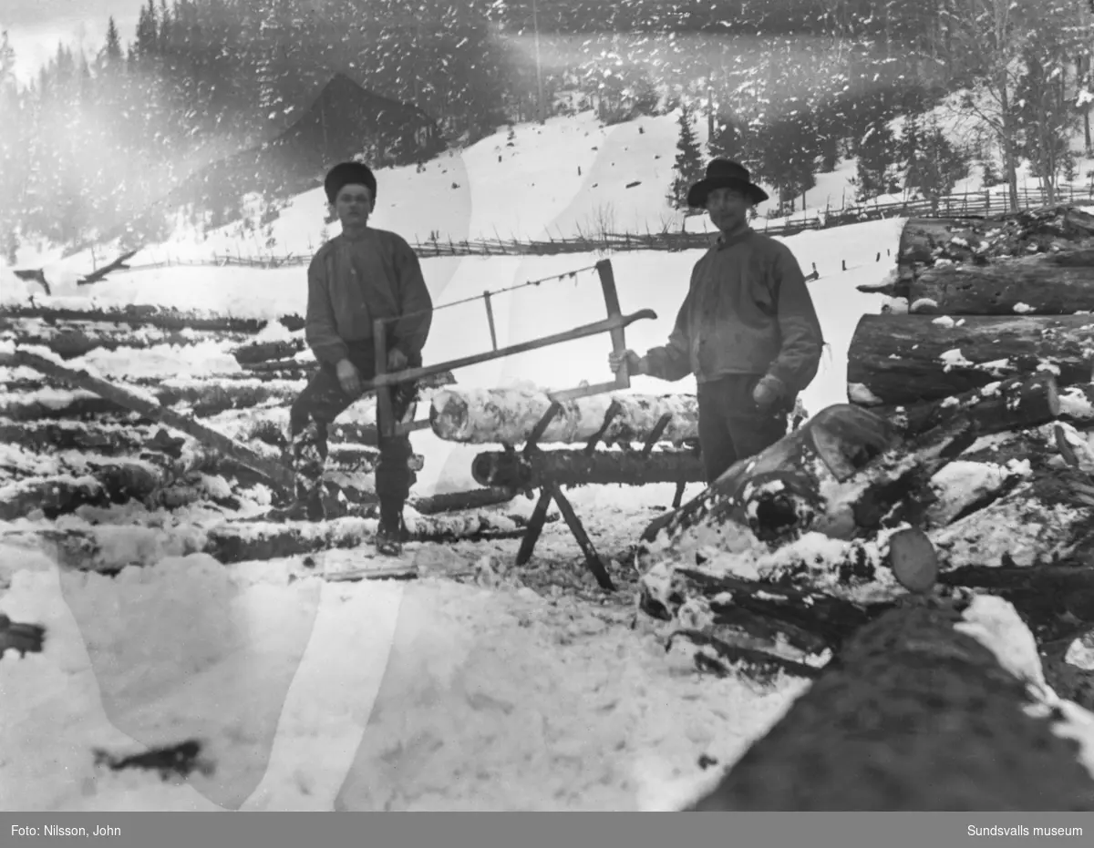 Två män jobbar med vedsågning på vintern, troligen vid någon av gårdarna på Roken, Laggarberg.