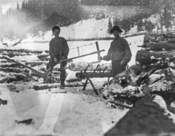 Två män jobbar med vedsågning på vintern, troligen vid någon