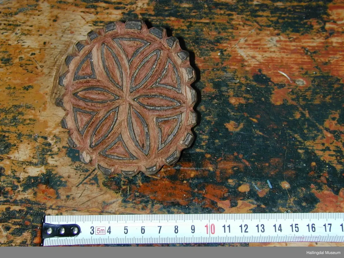 Lauvtre, skore rødbrun farget. 6- bladrose. skinnfelltrykk. Oval tagget kant. På baksiden hank med sirkulært hull.
25/6-68. O. Foldøy.