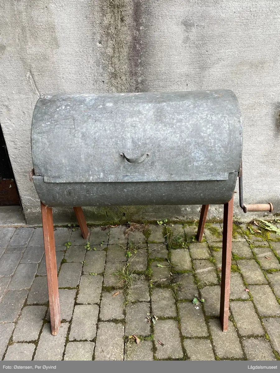 Hånddreven vaskemaskin utført i tre og blikk. Føtter, sider på vaskekassen og trommelen i kassen er utført i tre. Resten i blikk. Sveivestang i jern med dreid trehåndtak.  Vaskekassen er hengslet bak. Treverket er utvendig malt rødt og med logo for produsent på ene siden.