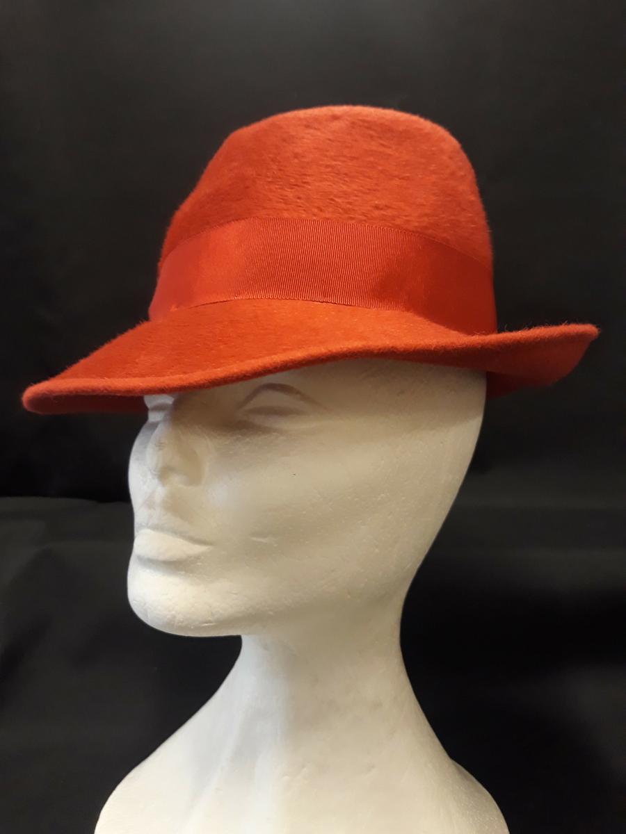 Rund hatt med høy pull og brem. Pyntet med ripsbånd og har også ripsbånd inni. Bremmen er brettet opp bak.