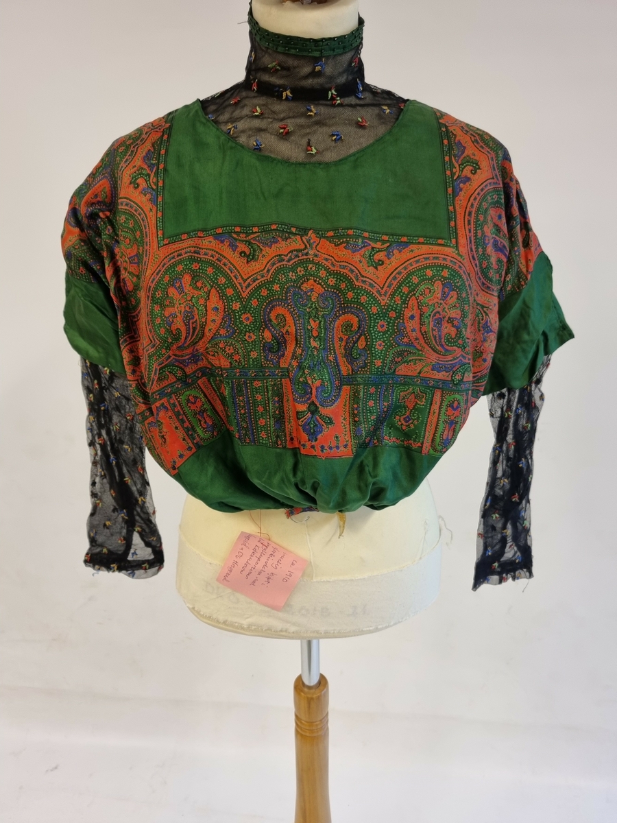 Posebluse med litt ståkrage og medlanage, trange ermer. Fòret og med lukning i ryggen.