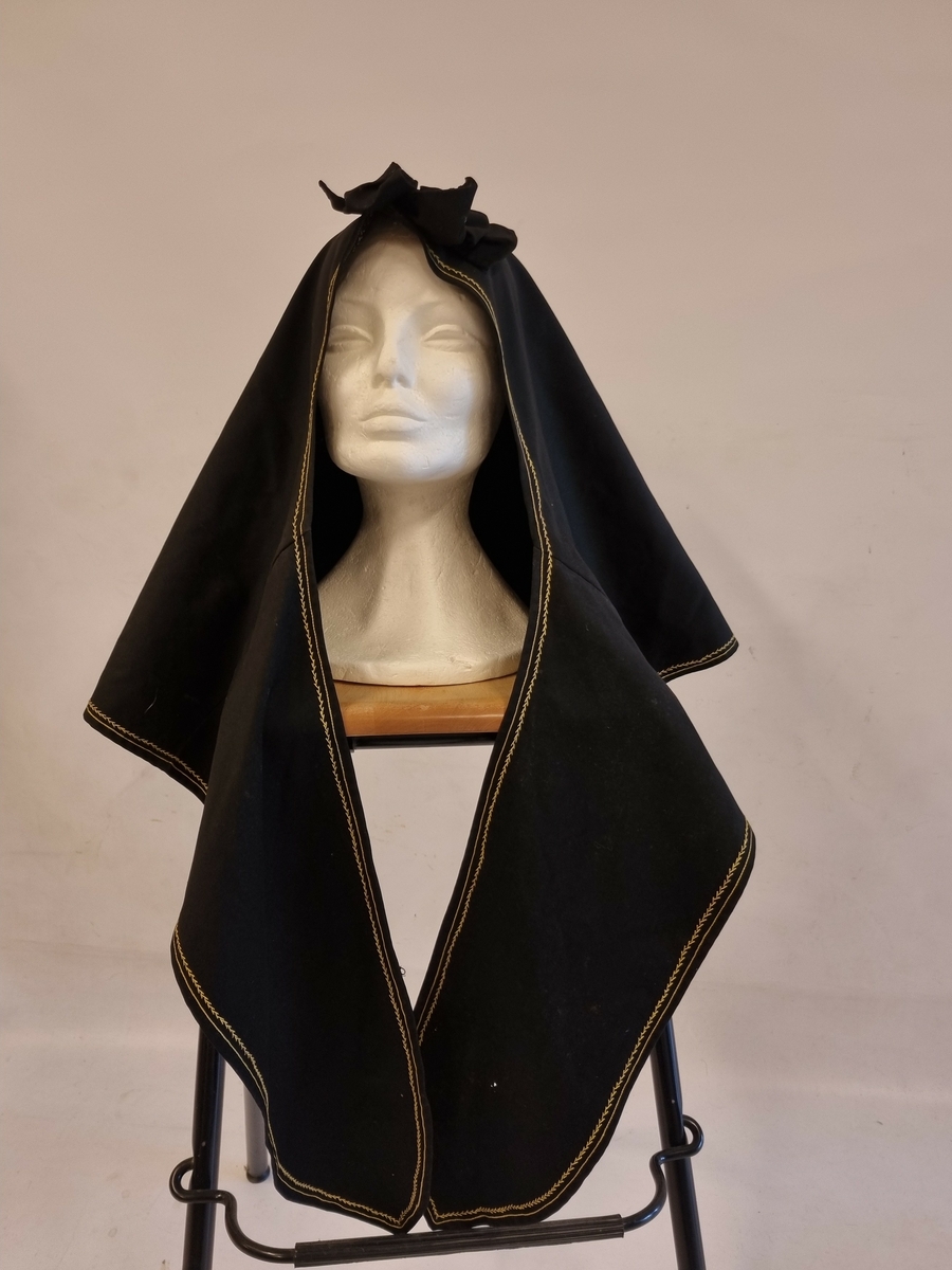 Stor hette med liten dusk bak. Hetta har sløyfe foran og kraftige "knytebånd". Pyntet med enkel broderikant.