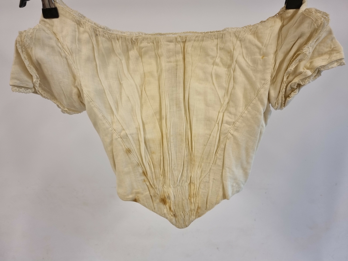 Tettsittende spileliv med hekter i ryggen. Korte ermer og rund hals. Smal blonde rundt hals og ermer.