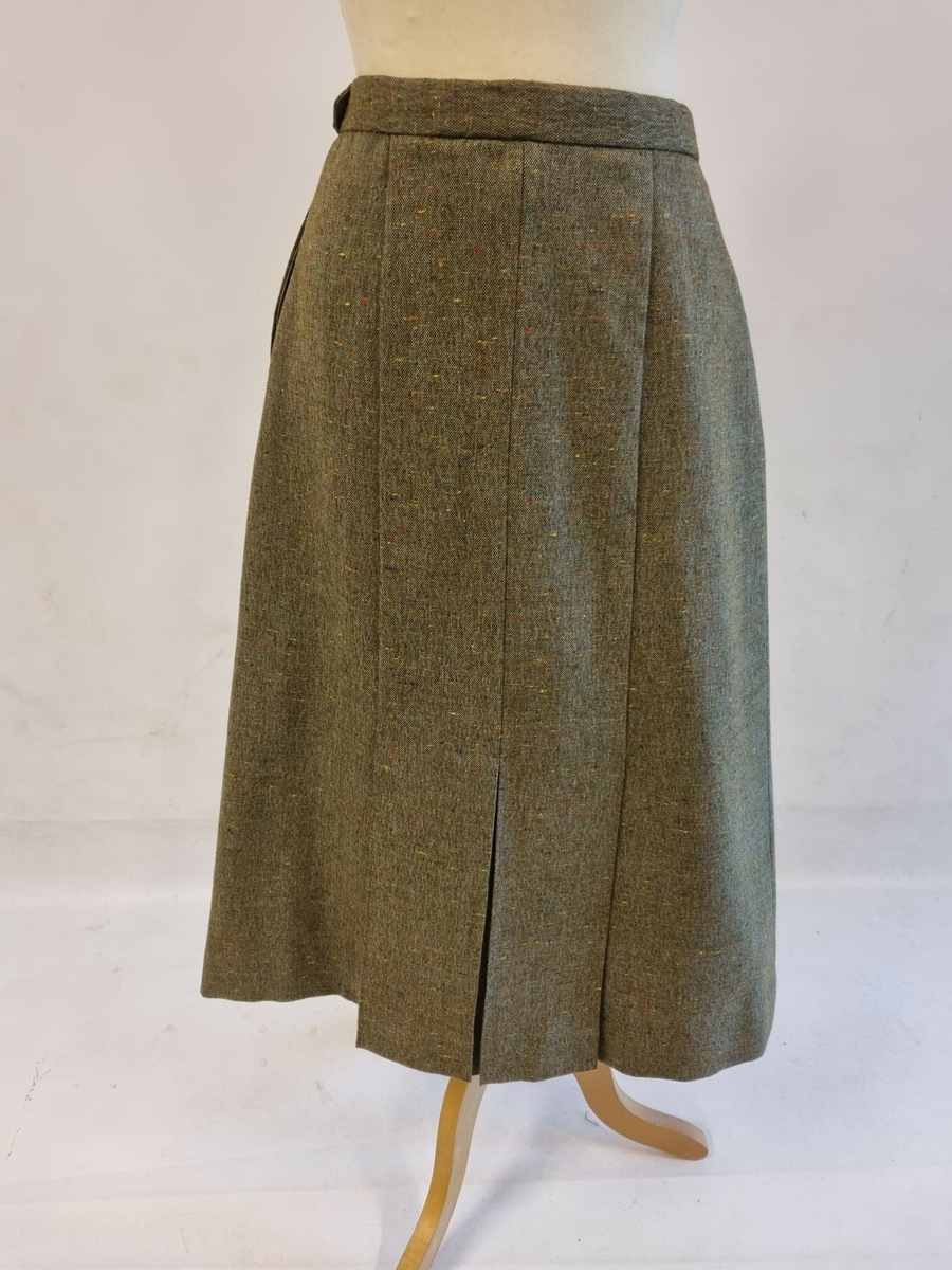 Draktskjørt med nedsydde folder foran og bak. Linning. Glidelås og knapp i siden. Konfeksjonssydd fra Joh. Kolstad, Oslo. Fra cca 1955.